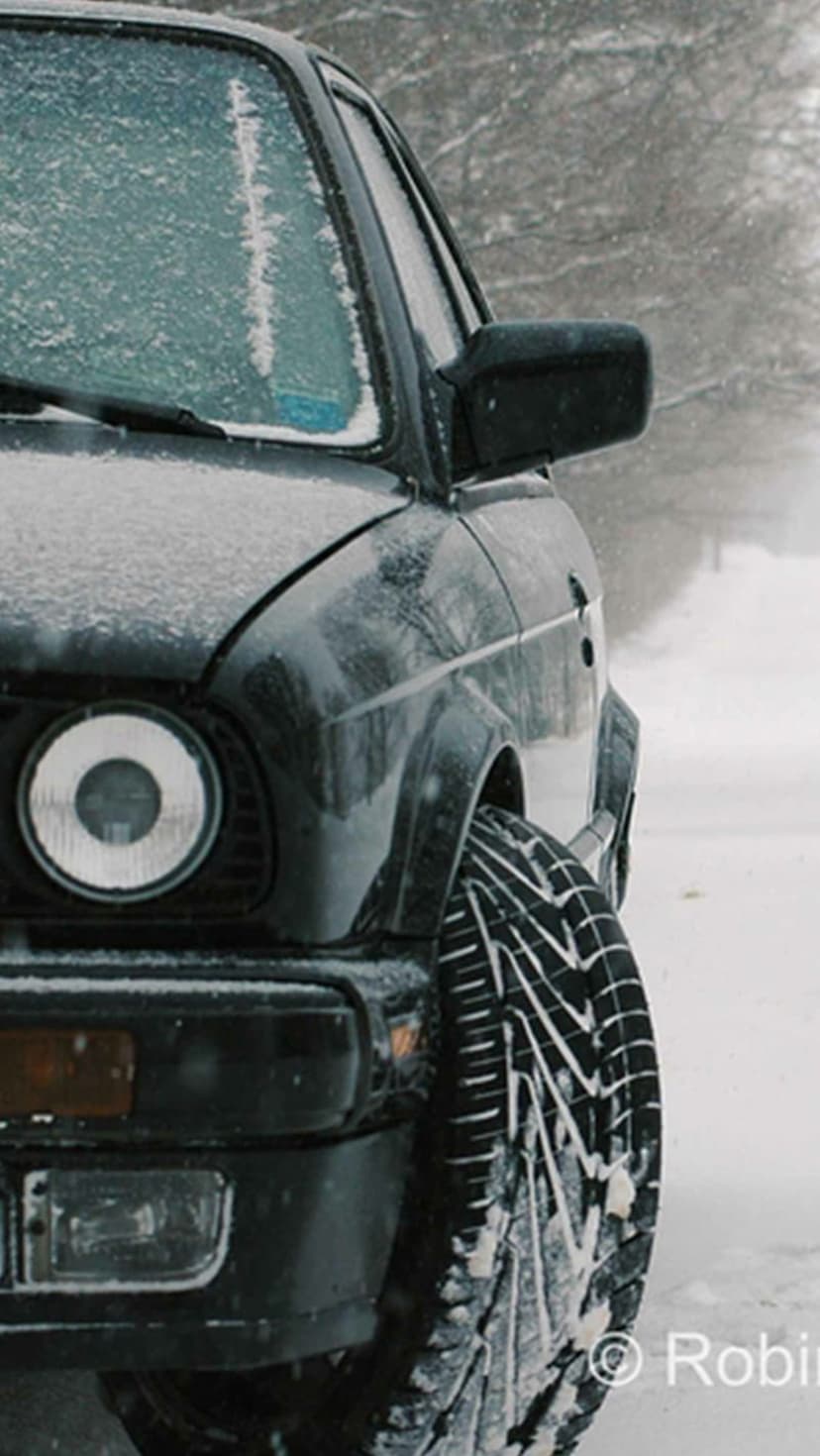 Vintage black car with a frost-covered windshield and textured tires parked in deep white snow during winter.
