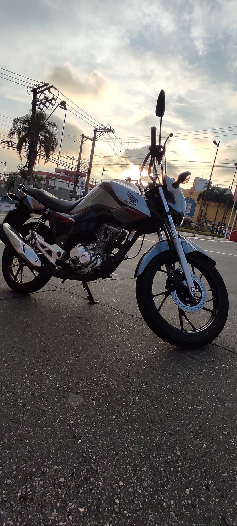 Honda motorcycle parked on reflective wet pavement beneath a cloudy orange sunset sky with distant power lines.