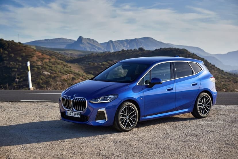 Blue BMW 2 Series Active Tourer parked on a gravel roadside with mountains and a clear sky behind it.