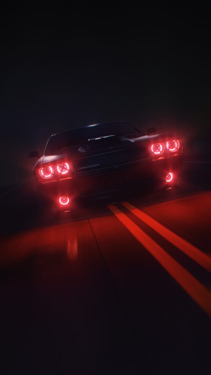 Dodge Challenger with glowing red halo headlights parked on a dark asphalt road with double yellow lines.