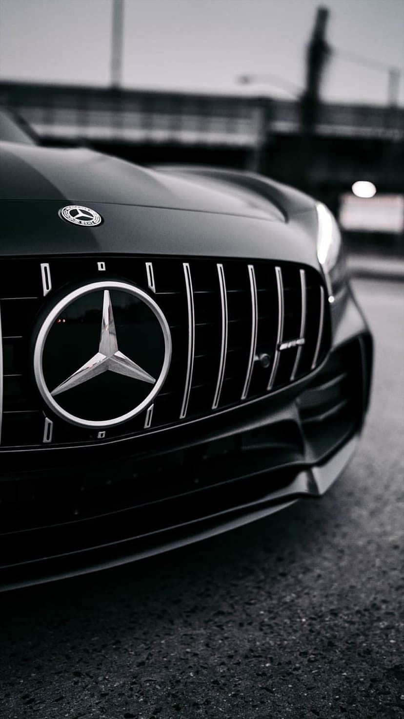 Mercedes-Benz star emblem and vertical AMG grille slats in a low-angle monochrome close-up with urban lighting.