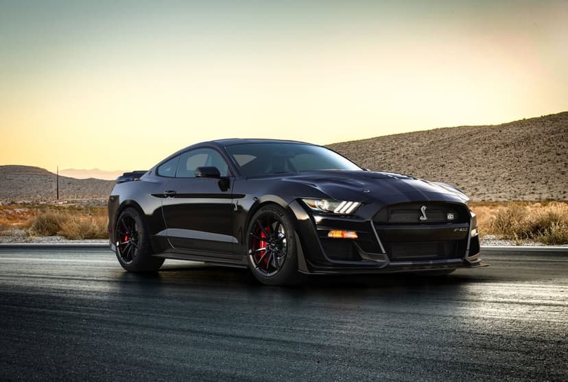 Black Shelby GT500KR sports car on an asphalt road with desert hills and golden sunset light in the background.
