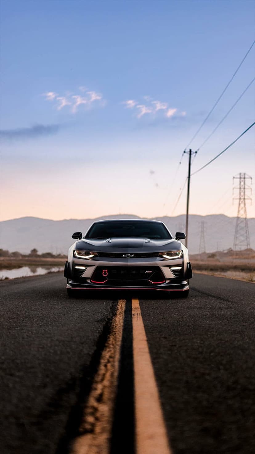 Black Chevrolet Camaro SS with red accents on a desert road under a colorful sunset sky during twilight.