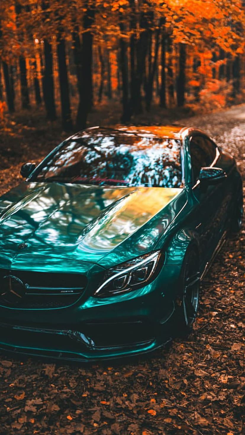 Green Mercedes-AMG C63 Coupe on a leafy road with orange autumn trees reflecting in the polished car body.