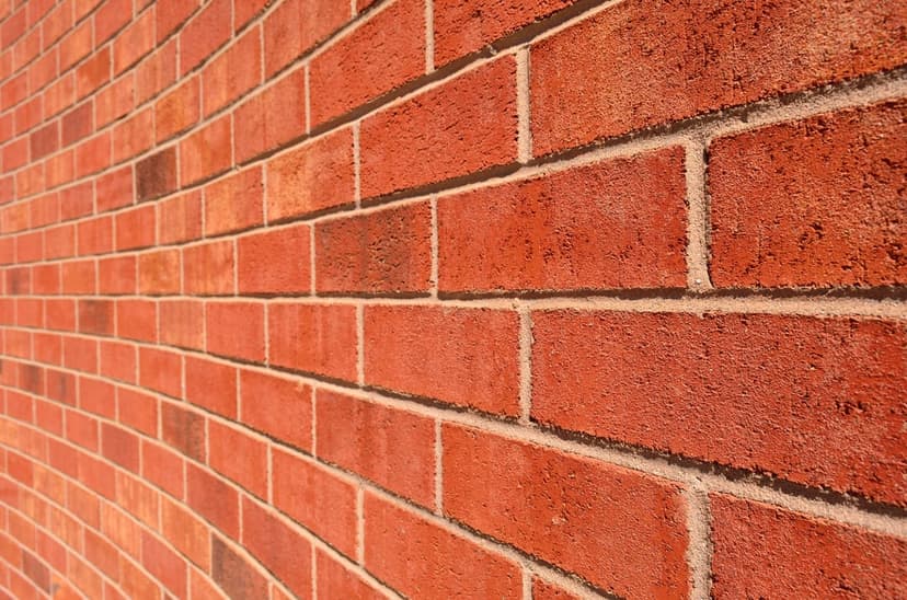Red brick masonry wall curves away from the viewer, highlighting the gritty texture of clay and mortar joints.