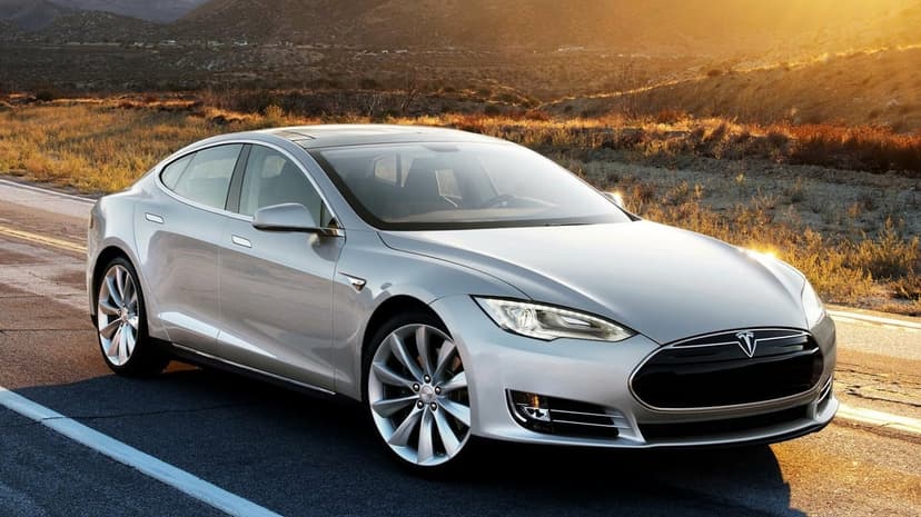 Silver Tesla Model S parked on a paved road during golden hour with mountains and sunset light in the background.