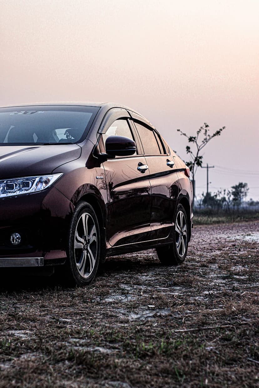 Maroon sedan parked on a dirt road at sunset with a silhouetted tree and hazy golden sky in the background.