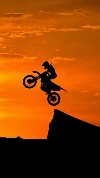 Motocross rider silhouetted against an orange sunset