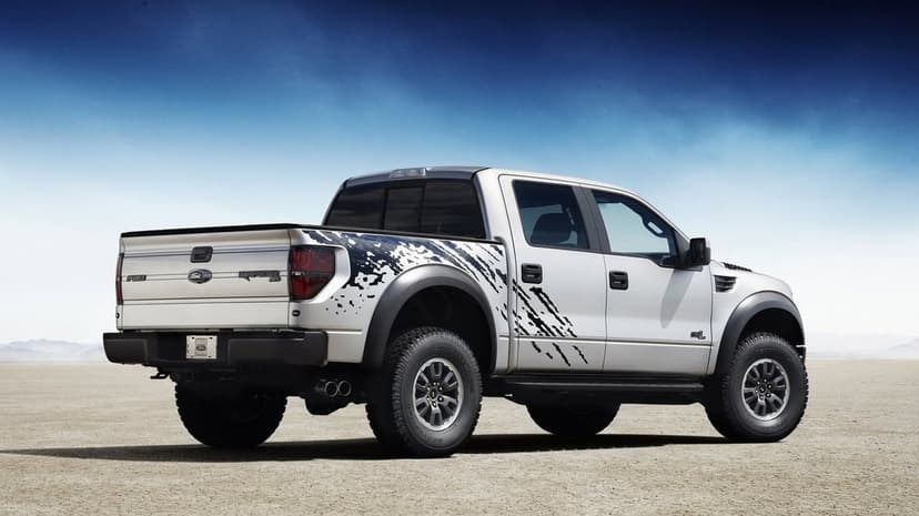 Silver Ford F-150 Raptor pickup truck with black decals parked on a dry desert salt flat under a clear blue sky.