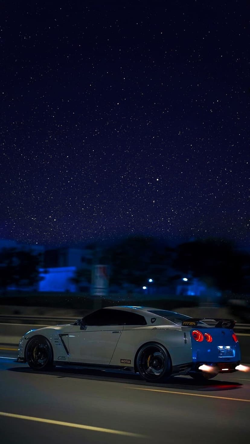 White Nissan GT-R sports car speeding at night with orange exhaust flames under a star-filled galaxy sky.