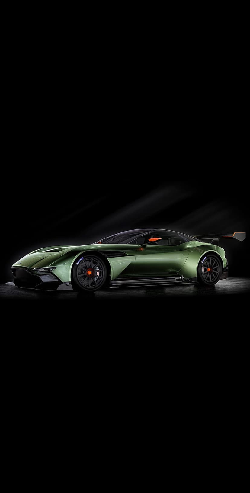 Emerald green Aston Martin Vulcan race car with a large rear wing and black wheels against a dark background.