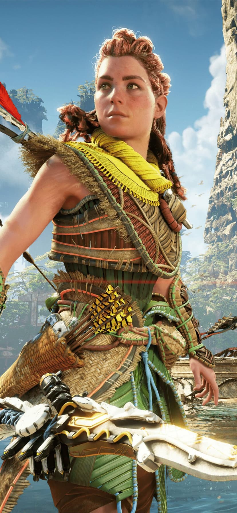 Aloy with red hair wearing yellow and green tribal armor standing before a tropical waterfall landscape.