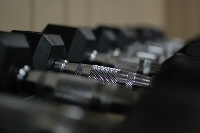 Chrome knurled dumbbell handles on a metal rack with a blurry gym background in a vertical close-up shot.