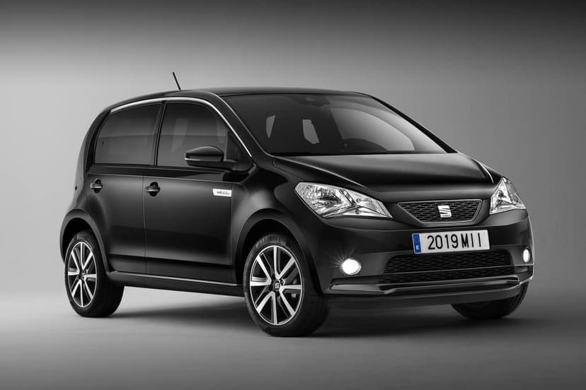 Black SEAT Mii Electric hatchback in a gray studio with glowing headlights and stylish alloy wheels.