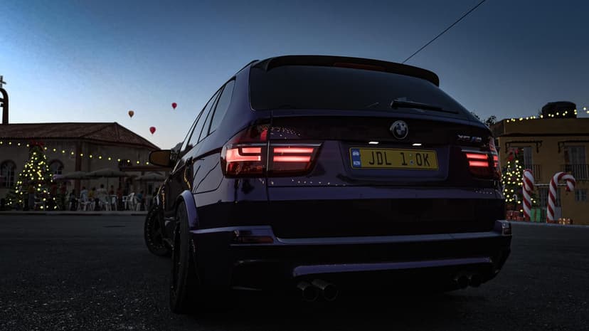 Rear view of a dark purple BMW SUV in a festive town square with Christmas trees and hot air balloons.