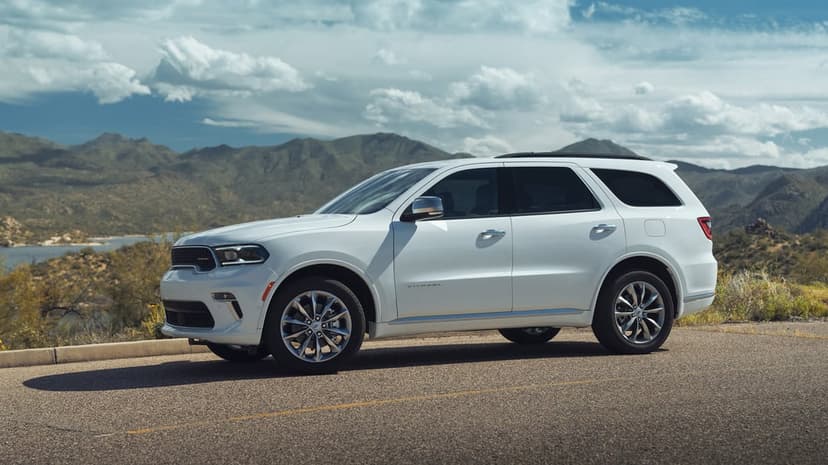 White Dodge Durango SUV on a desert road with rugged mountains and a cloudy blue sky in the background.