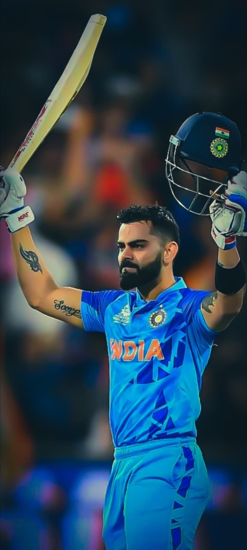 Virat Kohli raises a cricket bat and helmet while wearing a blue India jersey during a match victory celebration.
