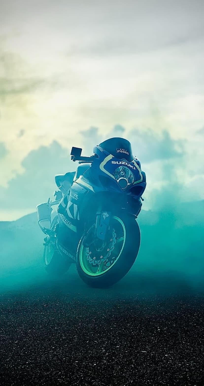 Suzuki sportbike racing through thick turquoise smoke and tire vapor against a dark and dramatic cloudy sky.