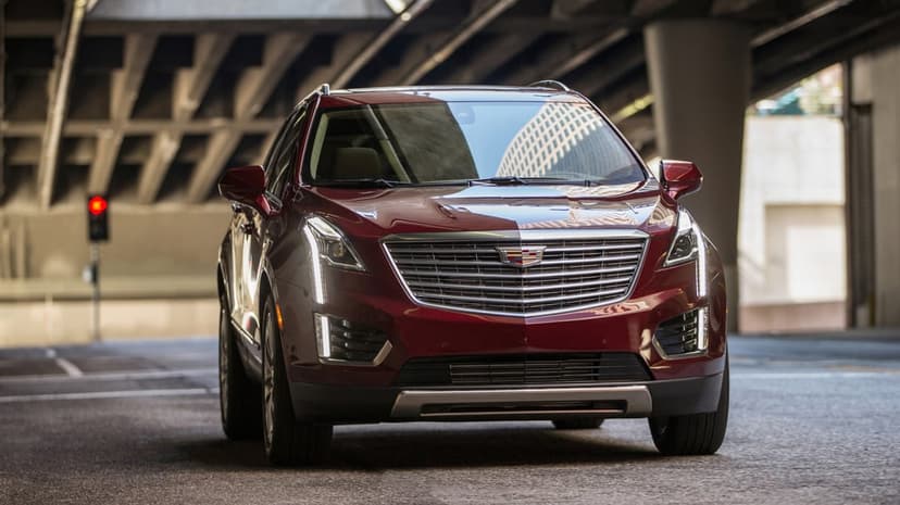 Maroon Cadillac XT5 SUV with vertical LED lights in an urban tunnel with concrete pillars and a red traffic light.