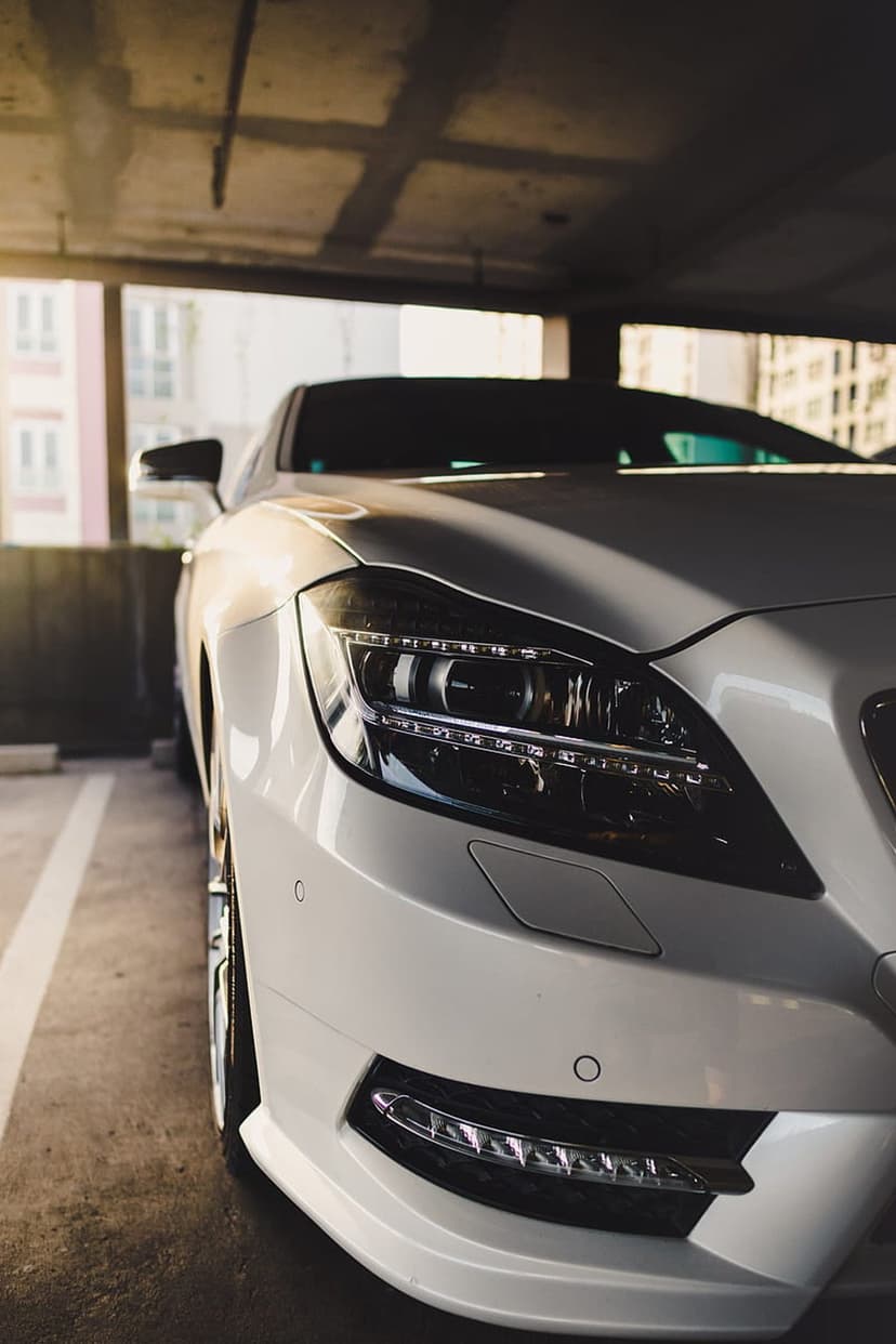White Mercedes-Benz CLS with glowing headlights parked on a concrete floor in a dimly lit industrial garage.