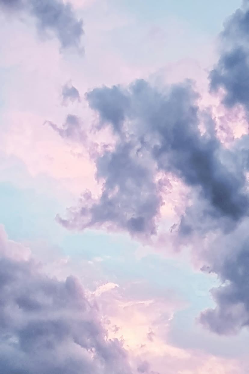 Pink and purple clouds float across a soft blue sky during a colorful sunset, creating a tranquil atmosphere.