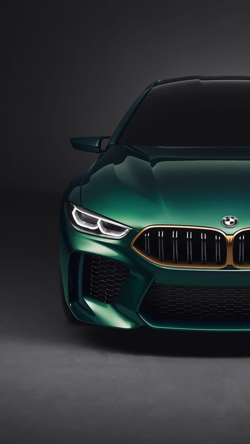 BMW M8 Coupe in emerald green features a gold kidney grille and sharp LED headlights on a dark background.