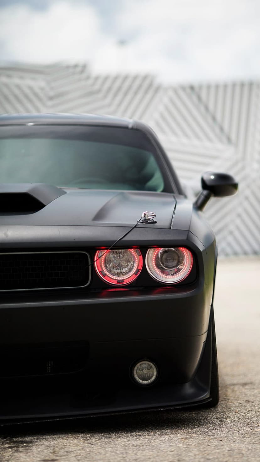 Dodge Challenger front end with red halo headlights and matte black paint against a geometric wall background.