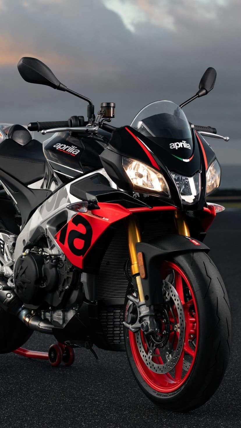 Aprilia Tuono V4 motorcycle with glowing headlights, red wheels, and gold forks on a dark asphalt track.