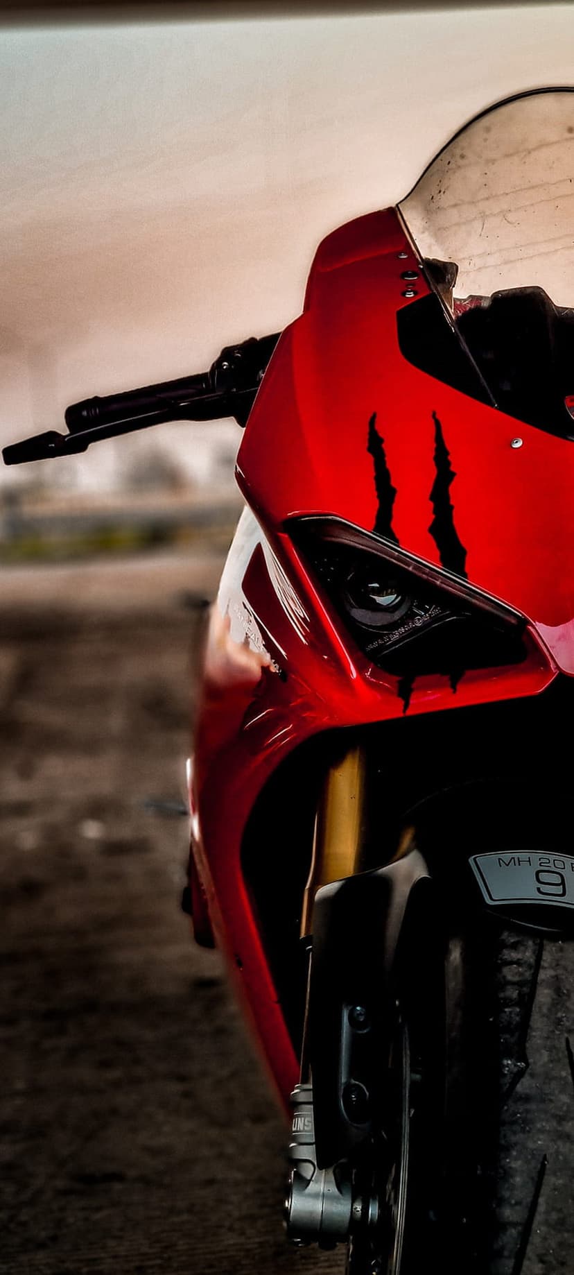 Red sportbike front fairing with black claw decals, a clear headlight, and a license plate reading MH 20.