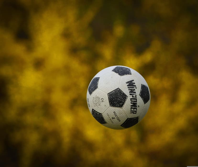 Soccer ball with black and white panels floats mid-air against a soft-focus, vibrant yellow background.