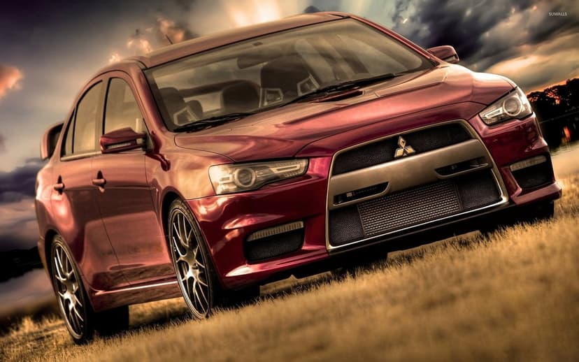 Red Mitsubishi Lancer Evolution X on a dry grassy field under a dramatic golden hour sky with low-angle framing.