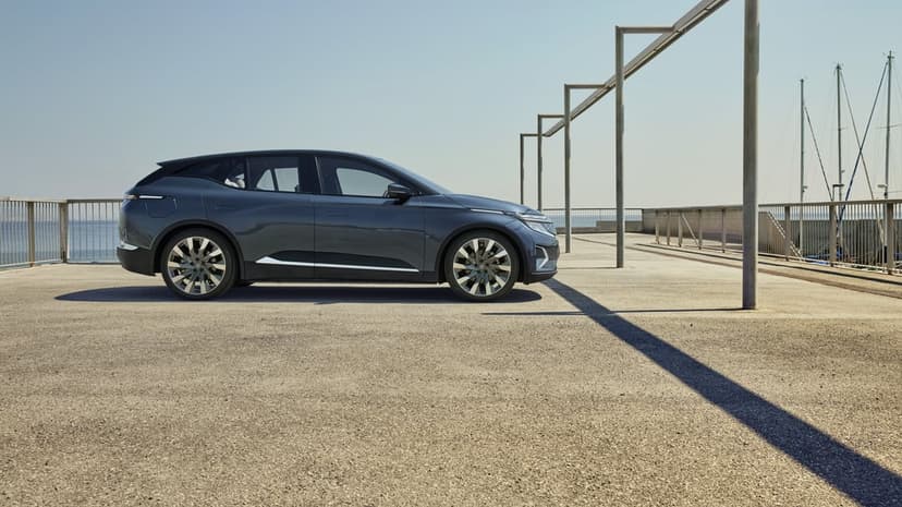 Dark grey electric SUV parked on a concrete pier with long geometric shadows under a clear blue sky.