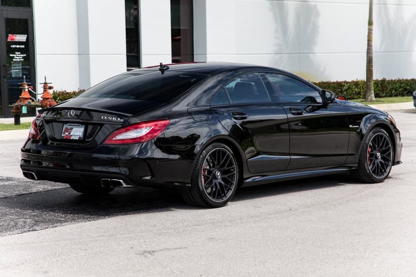 Black Mercedes-Benz CLS 63 AMG S-Model sedan parked on asphalt against a white building with palm tree shadows.