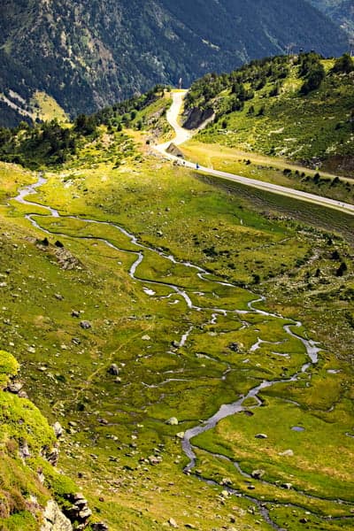 Meandering stream through green mountain valley with road