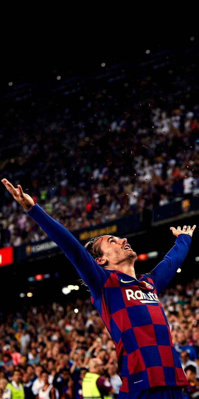 Antoine Griezmann raises his arms in celebration wearing a blue and red checkered jersey amid falling confetti.