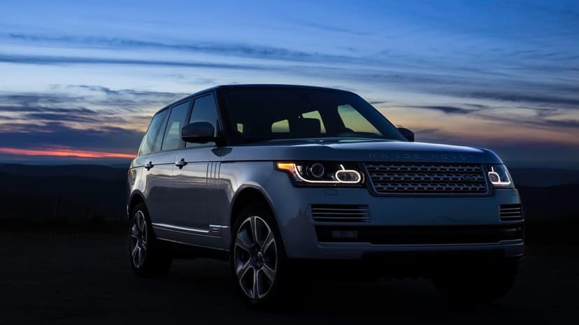 Silver Range Rover luxury SUV with glowing headlights parked against a twilight mountain sunset background.