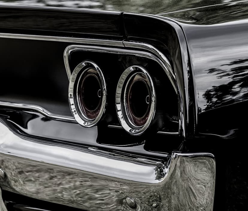 Dual red circular taillights and a polished chrome bumper on a glossy black vintage car in a vertical close-up.