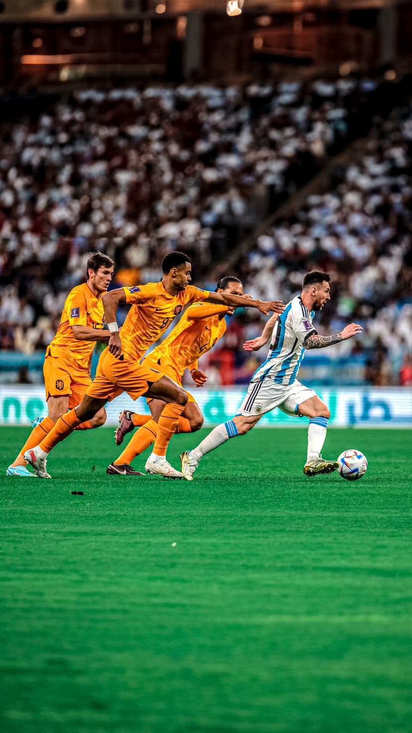 Lionel Messi dribbling a soccer ball past Dutch players in orange kits on a green field during a stadium match.