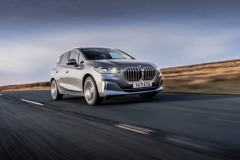Silver BMW 2 Series Active Tourer driving on a rural road with motion blur and a soft blue dawn sky background.