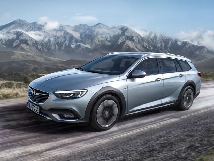 Silver Opel Insignia Country Tourer driving on a mountain road with a scenic peak backdrop and motion-blurred ground.