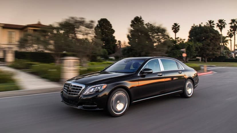 Black Mercedes-Maybach S-Class driving on a suburban road with golden hour sun reflections and motion blur.