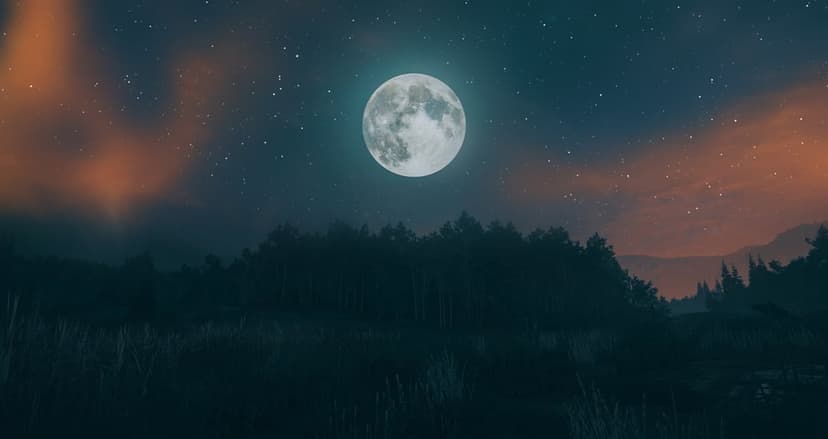 Radiant full moon hangs over a silhouetted treeline and meadow under a deep indigo sky with wispy clouds.