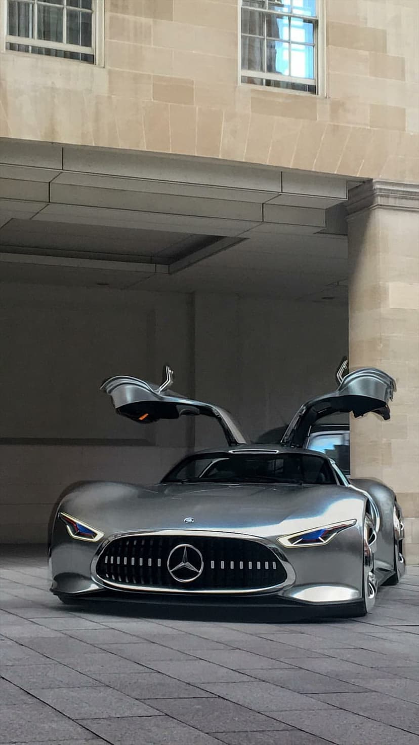 Silver Mercedes-Benz concept car with gullwing doors open against a backdrop of classical stone columns.