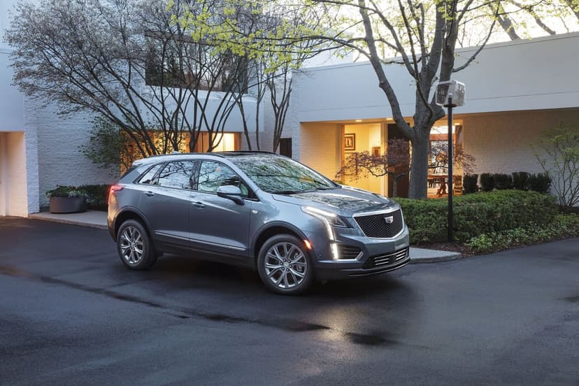 Silver Cadillac XT5 parked on a wet driveway in front of a modern house with glowing windows at dusk.
