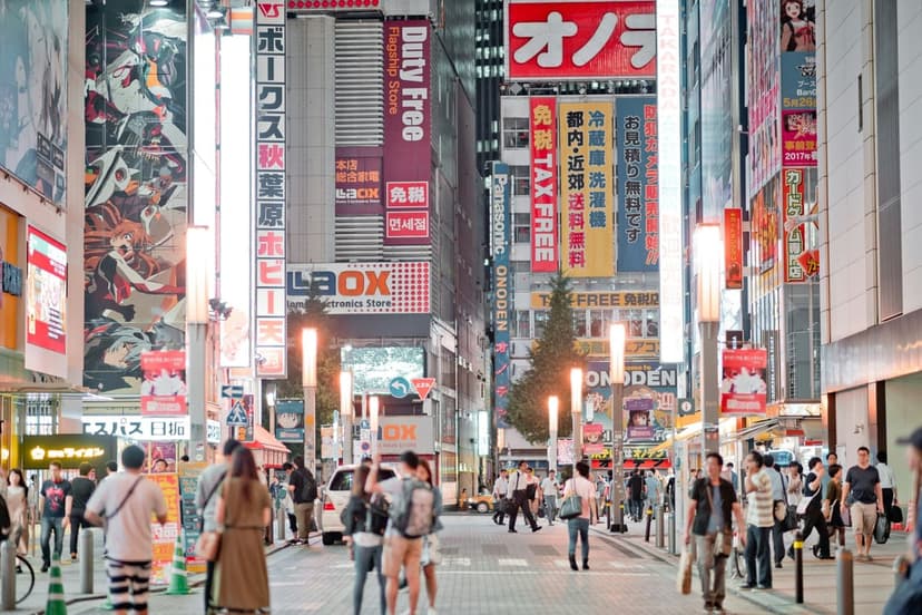 Akihabara buildings covered in colorful neon signs and Japanese text billboards under a twilight urban sky.