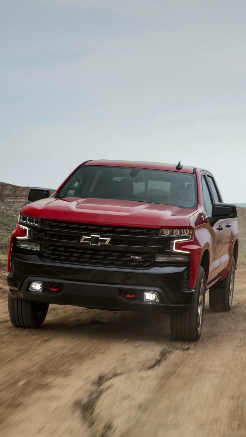 Red Chevrolet Silverado Z71 truck with a black grille and LED lights moving fast on a dusty off-road trail.