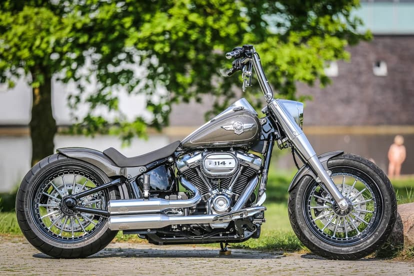 Side profile of a custom bronze Harley-Davidson Fat Boy motorcycle with chrome exhausts and ape hanger bars.