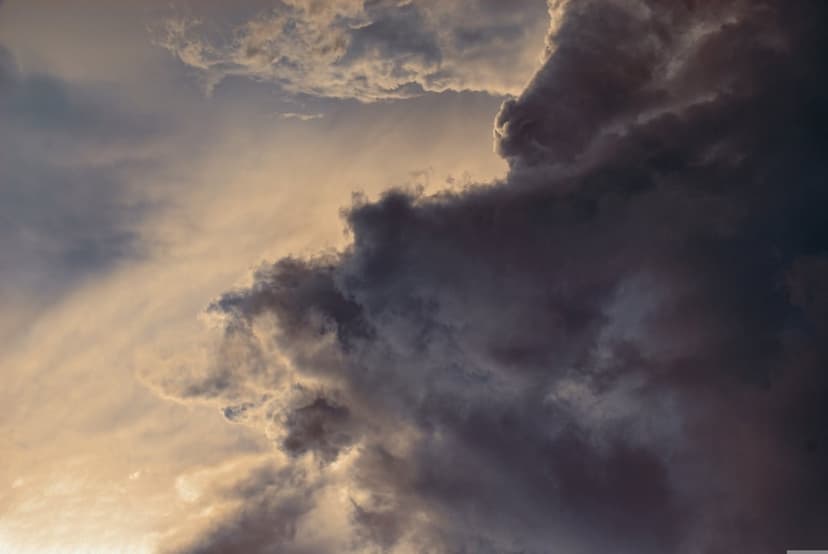 Dark storm clouds gather over a vibrant golden horizon during a dramatic sunset with heavy atmospheric contrast.