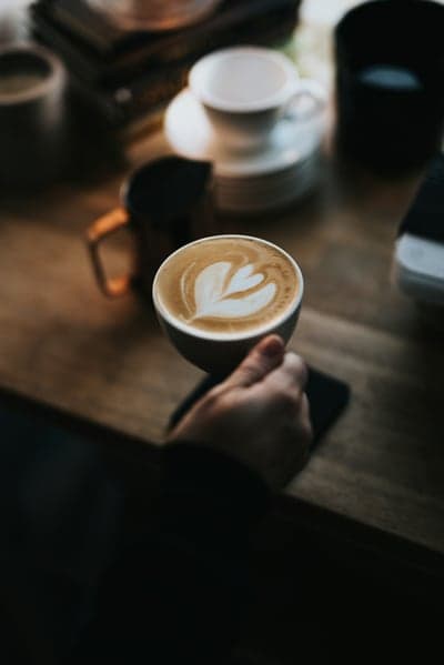 Latte art coffee cup held in hand over wooden table