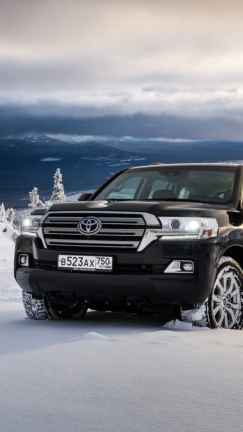 Black Toyota Land Cruiser SUV with license plate B523AX 750 driving through deep snow and mountain trees.